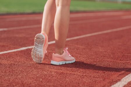 Girl legs in sport shoes standing on a running track with stadium stands. back view. close up.