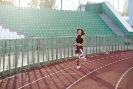 Sport. Athletic young brunette woman in pink sneakers, leggings and top run on running track stadium at sunset. her hair is developing. Concept run. concept of a healthy lifestyleの写真素材