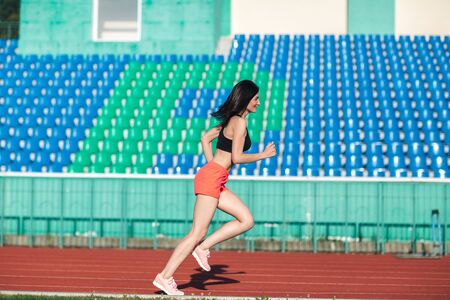 Girl running track on stadium. Real side view of young woman in pink shorts and tank top and pink sneakers. Outdoors, sport.の写真素材