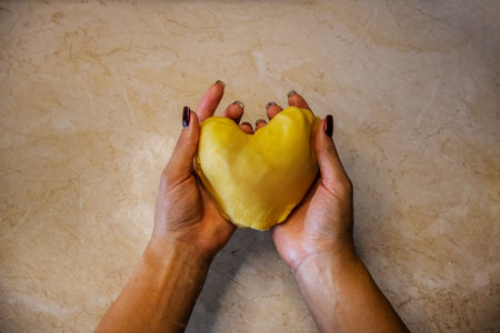 Woman's hands holding a yellow heart on a rustic background.の写真素材