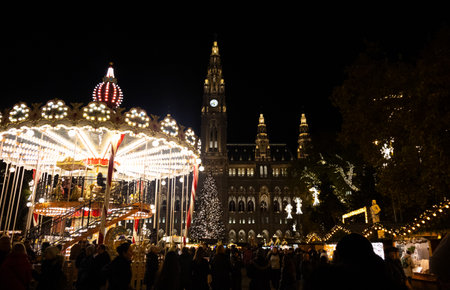 A Christmas market with an illuminated carousel, decorated tree, and a large castle, creating a magical and atmospheric holiday scene.の写真素材