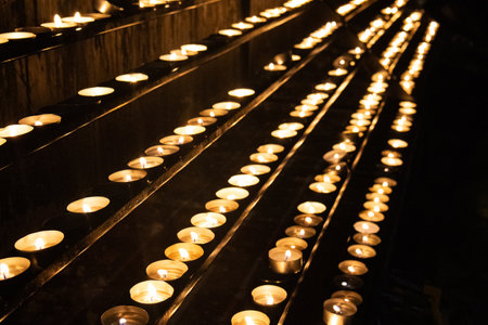 Various lighted candles on a platform in a church, creating a powerful contrast of light and dark, evoking a serene and contemplative atmosphere.の写真素材