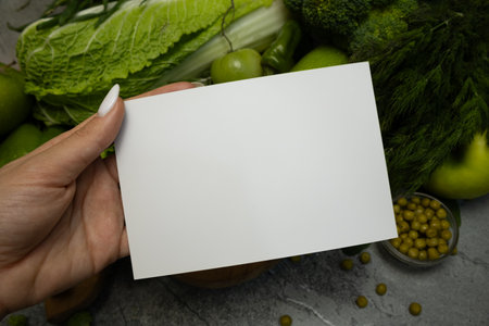 A card message held in a hand against a background of fresh green vegetables, emphasizing healthy eating and natural choices.の写真素材