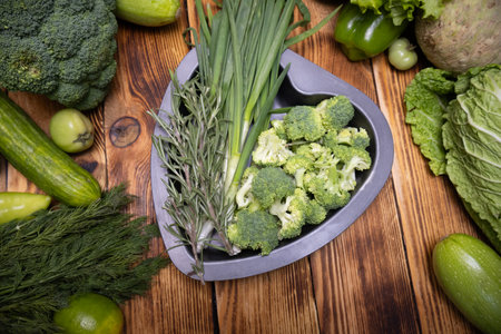 Green fresh vegetables arranged on a heart-shaped dish with a wooden background, symbolizing healthy eating and love for natural food.の写真素材