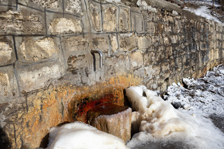A mountain water fountain surrounded by snow, showcasing a serene winter landscape with crystal-clear flowing water.の写真素材
