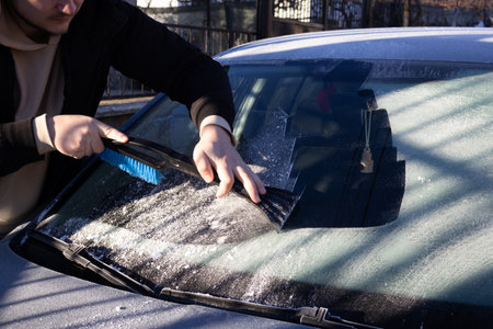 Man cleaning car windshield from ice using a scraper tool on a cold winter morning.の写真素材