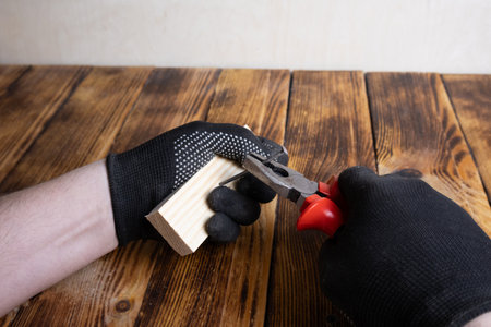 Male hands with gloves removing a nail from a piece of wood, close-up, carpentry, tool, DIY, repair,...