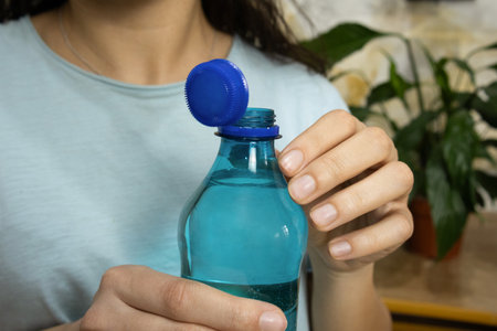 Opened bottle with stationary plastic cap and young woman in background, focus on bottle, blurred...