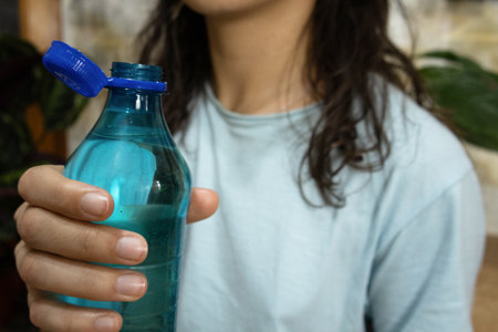 Bottle with stationary plastic cap in woman hand, focus on container, blurred backgroundの写真素材