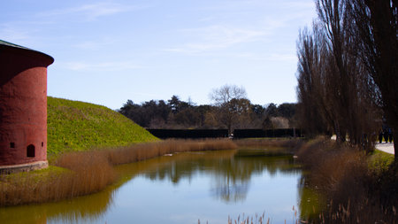 Spring rural landscape with a small river, bright blue sky, and white clouds reflecting in the water, showcasing serene nature.の写真素材