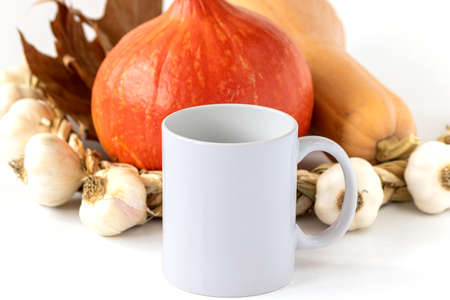 A closeup shot of a white mug, pumpkins and garlic on white background. Mockup scene.の写真素材