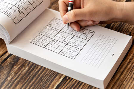 Person solving a sudoku puzzle on a wooden table.の写真素材