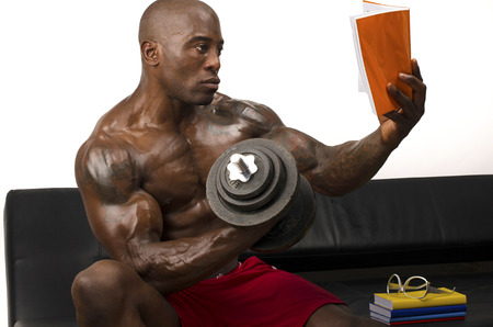 Bodybuilder training hard while reading a book. Strong man with perfect abs, pecs shoulders,biceps, tricepsの写真素材