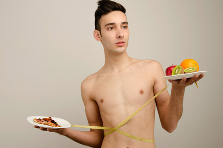 Man choosing between fruits, organic healthy food against pizza, fast food. Skinny anorexic man dieting and choosing what is healthy for himの写真素材