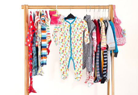 Dressing closet with clothes arranged on hangers.Colorful wardrobe of newborn,kids, toddlers, babies full of all clothes.Many t-shirts,pants, shirts,blouses,yellow hat,shoes, onesie hangingの写真素材