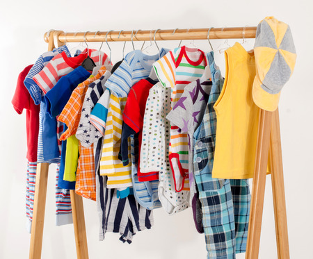 Dressing closet with clothes arranged on hangers.Colorful wardrobe of newborn,kids, toddlers, babies full of all clothes.Many t-shirts,pants, shirts,blouses,yellow hat, onesie hangingの写真素材