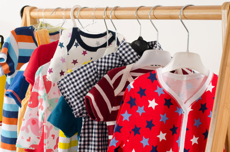 Dressing closet with clothes arranged on hangers.Colorful wardrobe of newborn,kids, toddlers, babies full of all clothes.Many t-shirts,pants, shirts,blouses, onesie hangingの写真素材