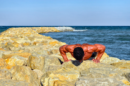 Strong bodybuilder with six pack.Fitness trainer with perfect abs, shoulders,biceps, triceps,chest, flexing his muscles on the beach, training in vacation, doing push ups in the sandの写真素材
