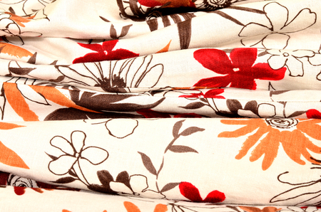 Folded fabric with red and orange flowers print on beige as background.の写真素材