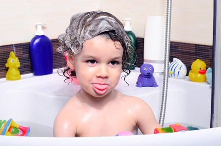 Beautiful toddler taking a bath in a bathtub with bubbles. Cute kid washing his hair with shampoo in the shower and splashing water everywhere. Boy playing with toys in the tubの写真素材