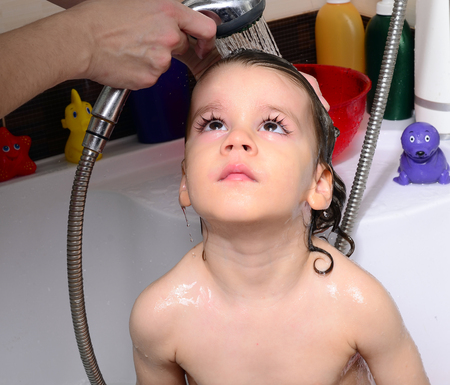 Beautiful toddler taking a bath in a bathtub with bubbles. Cute kid washing his hair with shampoo in the shower and splashing water everywhere. Boy playing with toys in the tubの写真素材