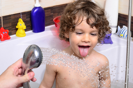Beautiful toddler taking a bath in a bathtub with bubbles. Cute kid washing his hair with shampoo in the shower and splashing water everywhere. Boy playing with toys in the tubの写真素材
