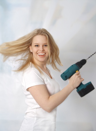 Portrait of a happy young woman posing with a drill against white backgroundの写真素材