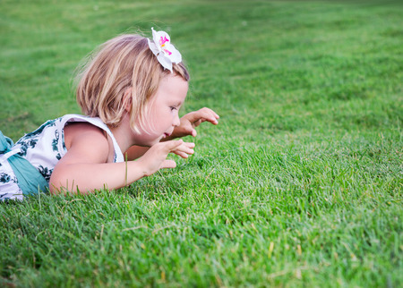Little beautiful girl  lies on the green grass outdoors in summer garden.の写真素材
