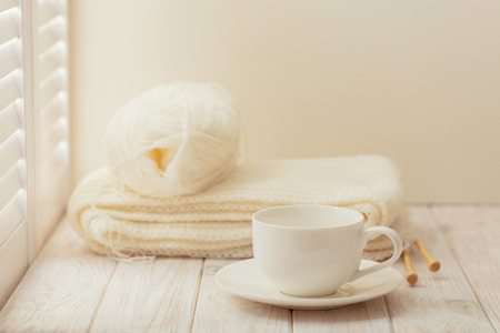 Knitting and a cup on a light wooden background near a window with shutters.の写真素材