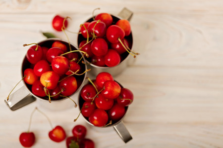 Cherries in metal mugs on a light wooden background. Selective focus.