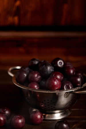 Ripe plums in a colander on a wooden background. Macro photo. Selective focus.の写真素材