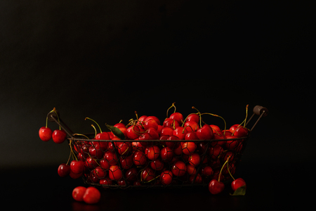 Cherries in a metal basket on a black background. Selective focus.の写真素材