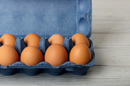 Chicken eggs in a blue package on a gray wooden background. Selective focus.