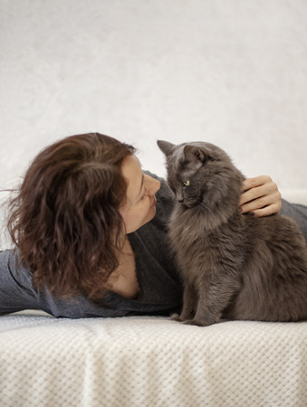 Young woman is resting on a sofa with her fluffy gray beautiful cat. Selective focus.の写真素材