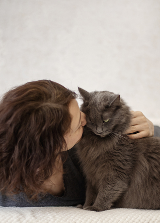 Young woman is resting on a sofa with her fluffy gray beautiful cat. Selective focus.の写真素材