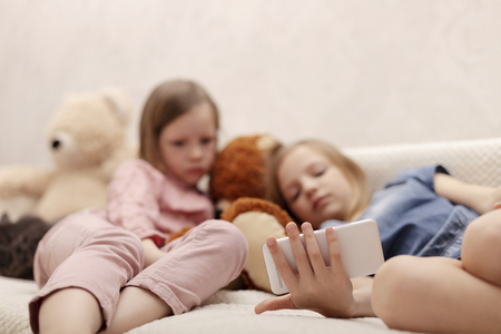 Two little girls (sisters 7 and 8 years old) are watching an e-book and a smartphone at home on the sofa with their cat. Selective focus.の写真素材