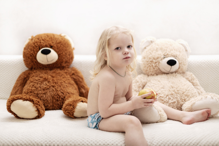 Little boy, three years old, plays and eats an apple on the sofa. Selective focus.の写真素材