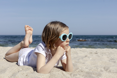 Funny little girl (7 years old) in sunglasses lies on the beach. Selective focus.の写真素材
