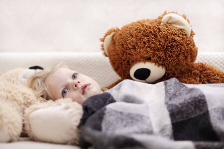 Small baby (a boy of three years old) is lying on the sofa under the rug with a teddy bear toys. Selective focus.の写真素材