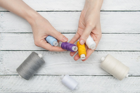 Women's hands hold colored thread for sewing on wooden white boards
