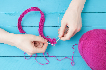 Knitting needles for knitting in the hands of a hank of pink yarn on wooden blue boardsの写真素材