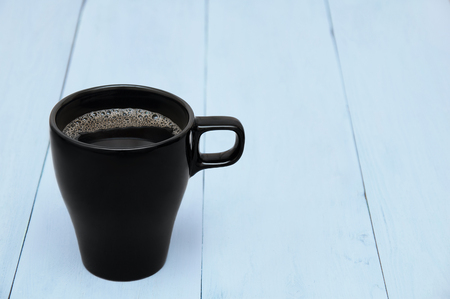 Black coffee cup with foam close-up on a blue wooden backgroundの写真素材