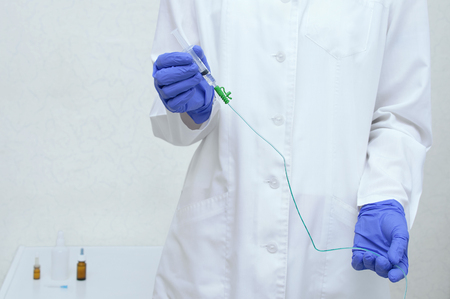 A urologist in a white lab coat and blue sterile gloves holds a catheter in his handsの写真素材