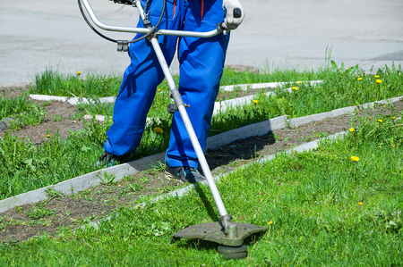 A man in working overalls mows the grass with a lawn mower. Close-up