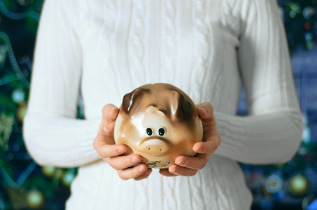A girl holds a piggy bank in the hands of a pig on the background of the Christmas tree.の写真素材