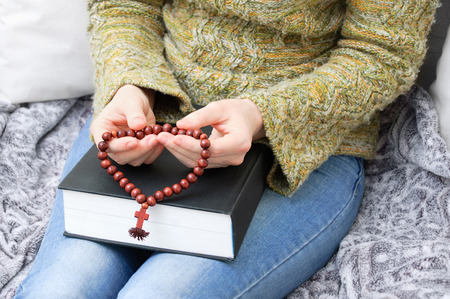 A girl in a green sweater is holding a bible and a wooden rosary with a cross.