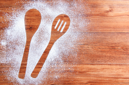 Wooden brown table dusted with flour. Silhouette of two spoons in flour.の写真素材