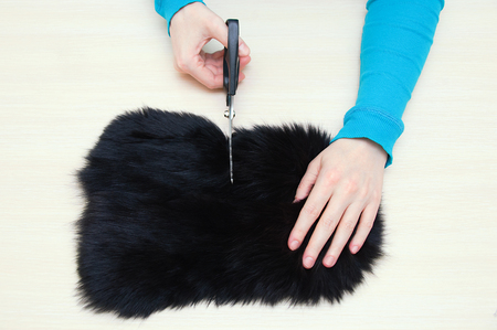 Caucasian girl cuts fur skin with black scissors on the table.View from above.の写真素材