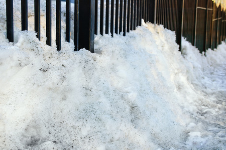 Spring. Melting snow. A snowdrift of dirty snow near a metal fence. Close-up.の写真素材