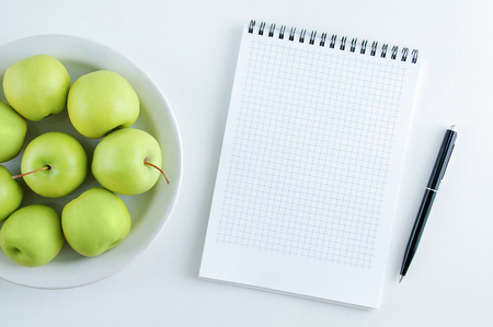 The concept of diet. Green apples on a white plate and a notebook with a pen. View from above.の写真素材